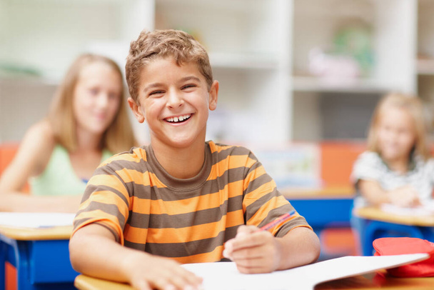 Enjoying a lighthearted moment in class. Sweet schoolboy sitting at his desk in class laughing happily. - Photo, image