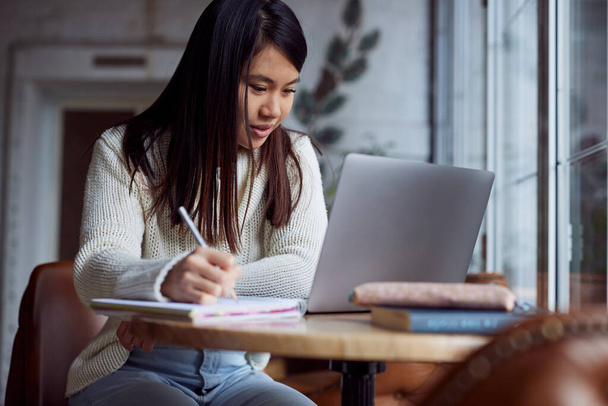 Uma estudante sorrindo está sentada em um café e estudando. - Foto, Imagem