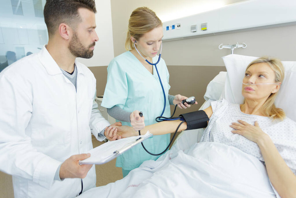female doctor checking blood pressure of senior woman in bed - Foto, Imagem