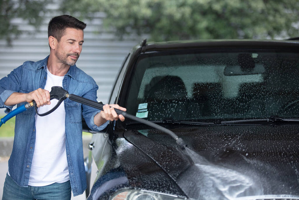 muž mytí jeho auto pod vysokým tlakem vody venku - Fotografie, Obrázek