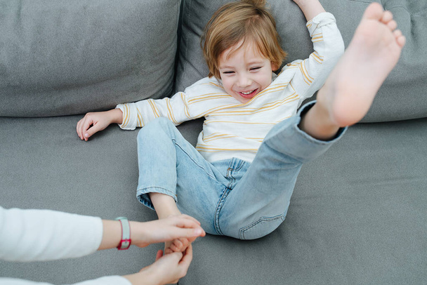 Squirming laughing boy being foot-tickled on the couch by girl's hands. - Foto, Bild