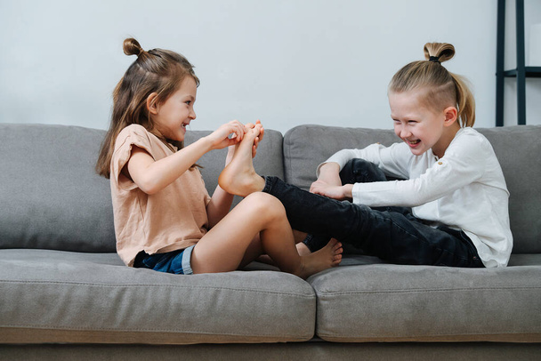 Little girl trying to tickle boy's foot, they both laugh. On the couch side view. - Photo, image