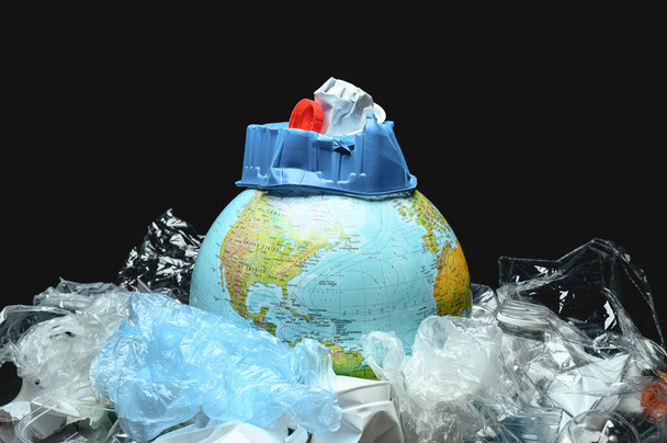 Глобус мира, окруженный пластиковым мусором на черном фоне. Концепция загрязнения Земли пластиком, полиэтиленом. - Фото, изображение
