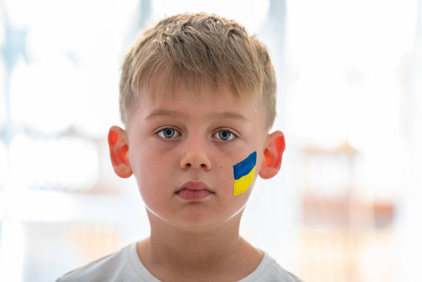 Kind gegen Krieg. Aufgebrachter ukrainischer Junge mit bue gelber Flagge im Gesicht, der gegen den Krieg protestiert. Evakuierung von Zivilisten. Freiheit für die Ukraine. Stoppt die russische Aggression. Stoppt den Krieg Ukraine Russland. Unterstützung der Ukraine - Foto, Bild