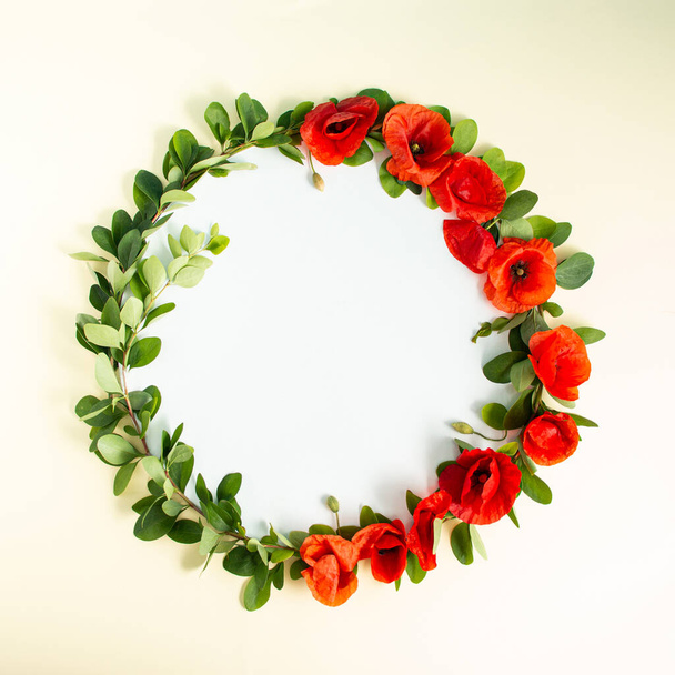 Corona de marco redondo con flores de amapolas rojas y ramas sobre fondo arenoso. Composición floral mínima. Acostado. Copiar espacio. - Foto, imagen