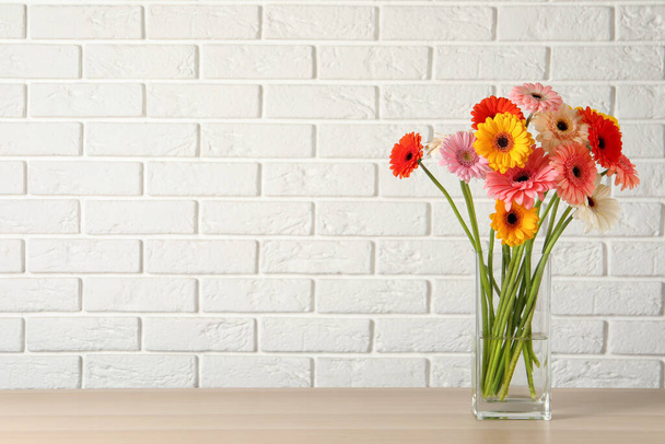 Bouquet of beautiful colorful gerbera flowers in vase on table against white brick wall. Space for text - Fotó, kép