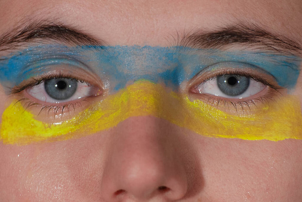 Colores de la bandera ucraniana pintados en la mirada de tristes ojos azules llorando. - Foto, imagen