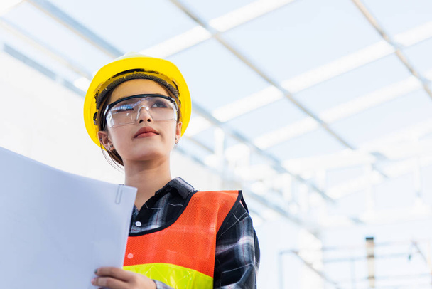 Asian engineer architect worker woman holding blueprint infrastructure progress at construction site, engineering female leader standing hold paper plan control worker to building project - Fotó, kép