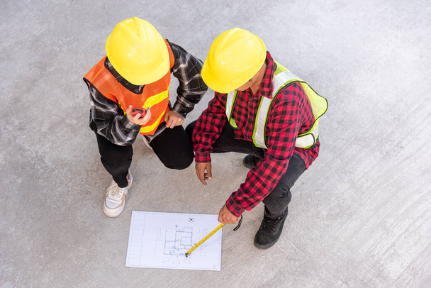 Architect and client discuss help create plan with blueprint of the building at construction site floor. Asian engineer foreman worker man and woman meeting talking on drawing paper project, top view - Photo, image