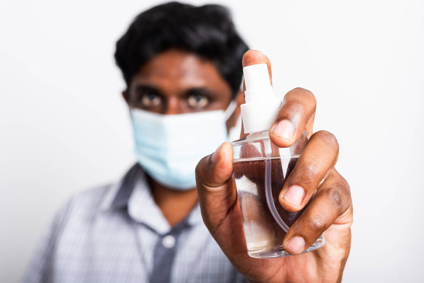 Closeup Asian black man wearing protective face mask fear in eye holding show sanitizer spray, hygiene prevention COVID-19 virus or coronavirus protection concept isolated on white background - Foto, Imagen