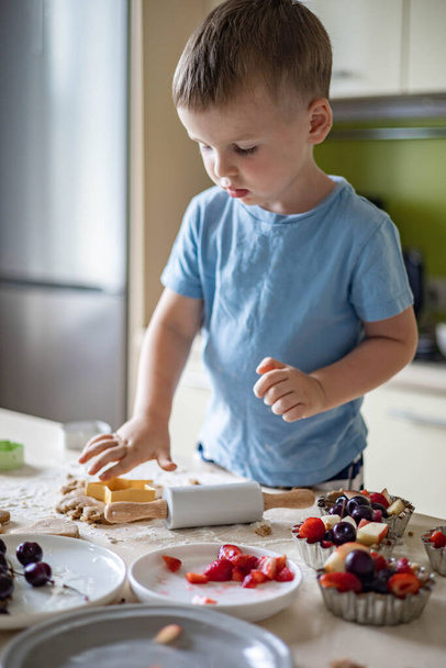 Cheerful male baby cooking homemade summer dessert with fruits and berries at home kitchen - Zdjęcie, obraz