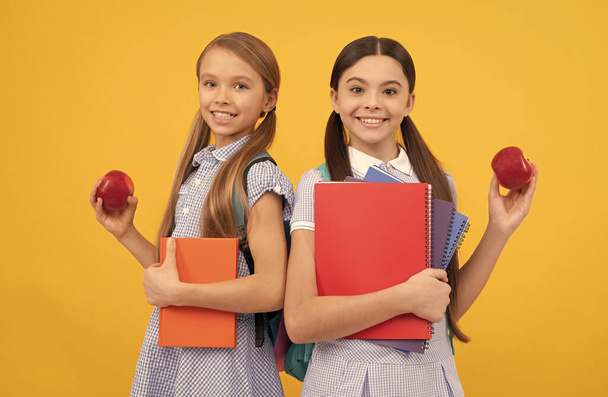 Happy pupils with books hold vitamin organic apples yellow background, school breakfast - Photo, Image