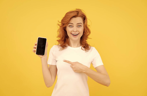 興奮した若い女性は、 okジェスチャーを示す携帯電話を使用して黄色の背景を隔離. - 写真・画像