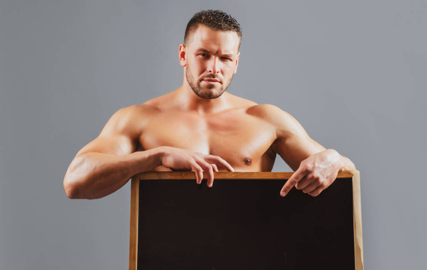 Advertising concept. Fitness man with sign board. Strong bodybuilder holding blank poster. Handsome muscular man holding and looking at camera. - Фото, зображення