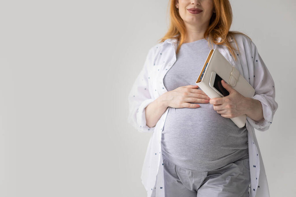 Smiling young pregnant business woman talking smartphone holding diary and laptop - Foto, Imagen