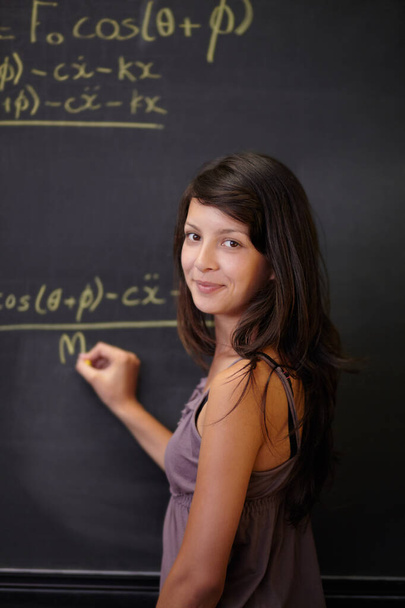 Showing her methodology. A young attractive Indian woman, solving a maths problem on the blackboard in class. - Fotó, kép