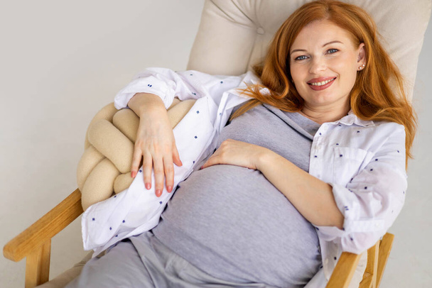 Draufsicht glücklich junge rothaarige schwangere Frau liegt auf bequemen Sessel - Foto, Bild