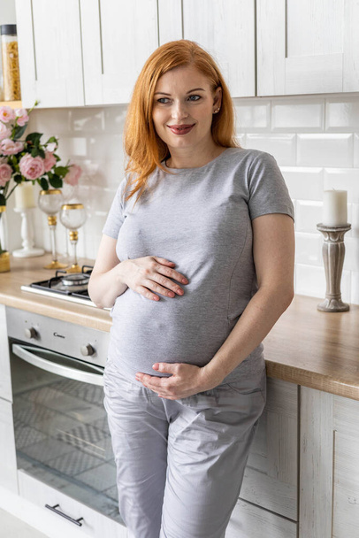 Happy pregnant woman posing with coffee tea mug in modern minimalistic nordic kitchen at home - Foto, Imagem