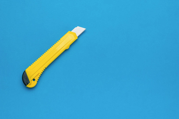 Parlak mavi bir arka planda sarı kırtasiye bıçağı. Asgari konsept. - Fotoğraf, Görsel