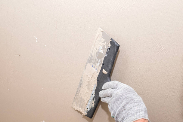 Mann verputzt Wand mit Spachtelmesser, Vorbereitung für Anstrich.Hände des Arbeiters mit Putzwerkzeugen renovieren Haus. Putzer saniert Wände und Ecken mit Spachtel - Foto, Bild