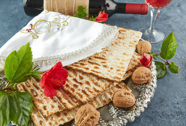 Pesach celebration concept - jewish Passover holiday. Matzah on traditional Seder plate with bottle of red wine, glass of wine, nuts and flowers. Close up - Photo, Image