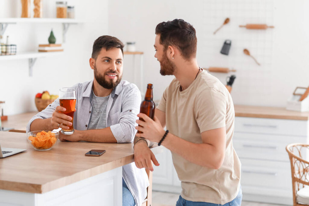 Amigos varones con cerveza y patatas fritas sentados a la mesa en la cocina - Foto, imagen