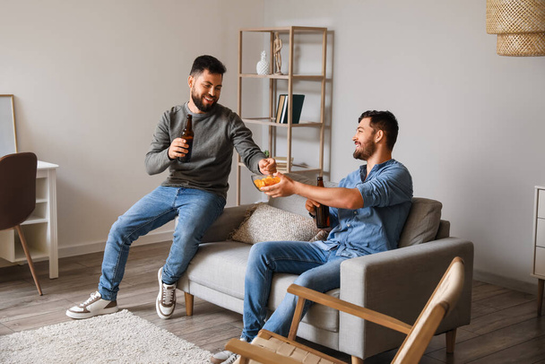 Mannelijke vrienden die thuis bier drinken op de bank - Foto, afbeelding