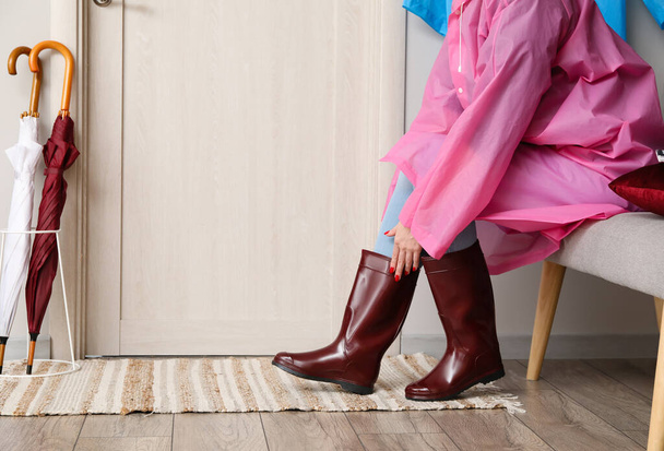 Kobieta zakładająca gumowe buty na korytarzu - Zdjęcie, obraz