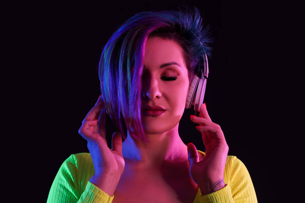 Красивая женщина с необычными волосами слушает музыку на черном фоне - Фото, изображение