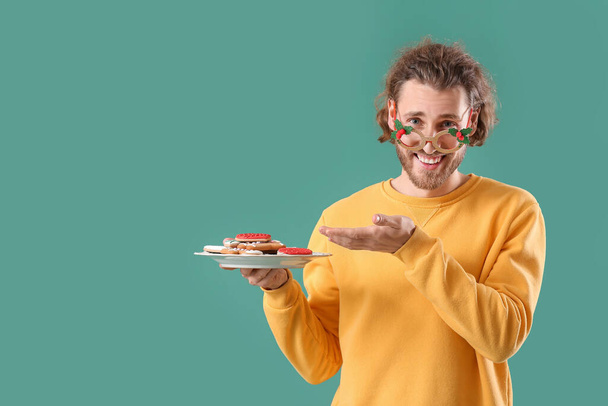 Noel dekorunda yakışıklı bir adam elinde yeşil arka planda zencefilli kurabiye tabağıyla - Fotoğraf, Görsel
