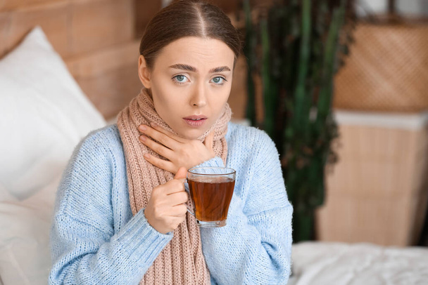 Плохая молодая женщина с больным горлом пьет горячий чай дома - Фото, изображение