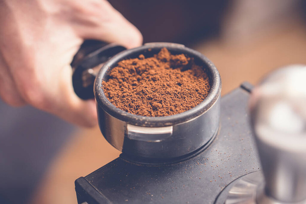 Barista holding portafilter with fresh coffee in hand preparing press coffee with tamper. Close up - Foto, Bild