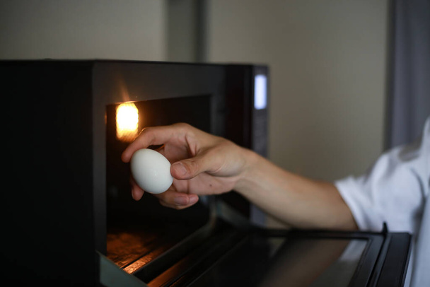 Ein Mann versucht ein Ei in der Mikrowelle zu erhitzen - Foto, Bild