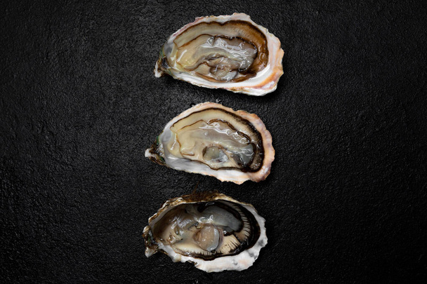 Sea delicacy fresh open oysters are laid out on a dark background. - Фото, изображение