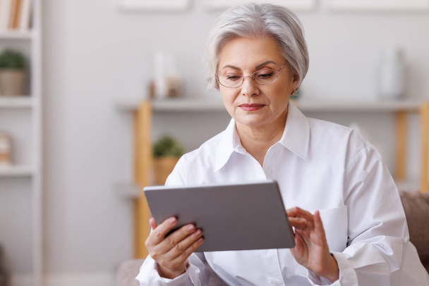 Focused mature woman using tablet at home - Φωτογραφία, εικόνα