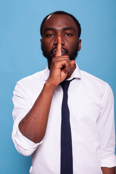 Porträt eines afrikanisch-amerikanischen Mannes, der mit dem Zeigefinger über den Lippen ein Schweigezeichen macht - Foto, Bild