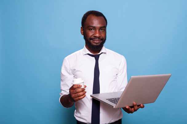 Портрет улыбающегося бухгалтера, смотрящего в камеру с ноутбуком и чашкой горячего напитка - Фото, изображение