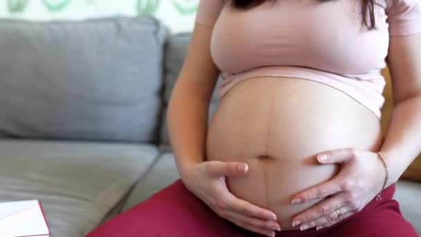  Una mujer embarazada acariciando suavemente su gran barriga en casa. El concepto de esperar a un niño, embarazo y atención prenatal de maternidad - Imágenes, Vídeo