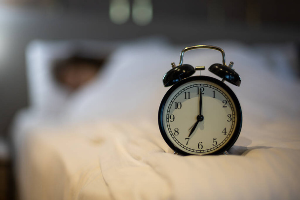 Alarm clock on bed with sleeping woman behind. - Foto, imagen
