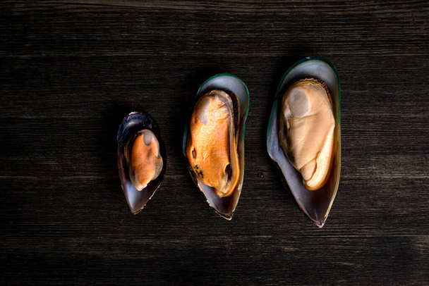 cooked mussels of different sizes on a wooden background - Zdjęcie, obraz