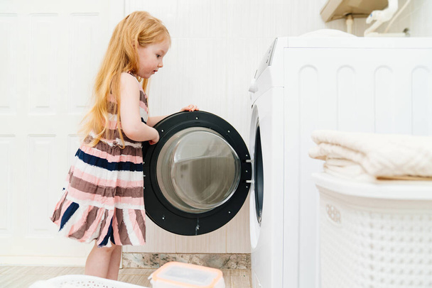 a cute little girl closes or opens the washing machine door. - Foto, Imagem