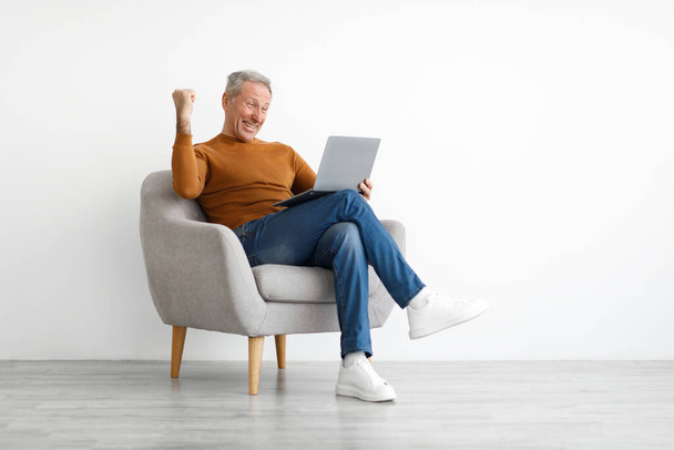 Mature homme utilisant un ordinateur portable célébrant le succès en secouant les poings - Photo, image