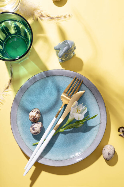  Table setting for celebrating easter. Plate, cutlery, eggs and spring flowers on the yellow table top view, vertical photo - Zdjęcie, obraz