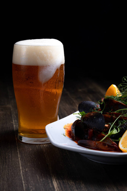 beer with mussels in tomato sauce with microgreens and lemon, on a wooden background - Photo, image