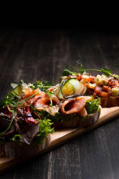 a dish of 3 different tapas stuffed with meat, fish and various microgreens, served on a board against a dark background - Foto, imagen