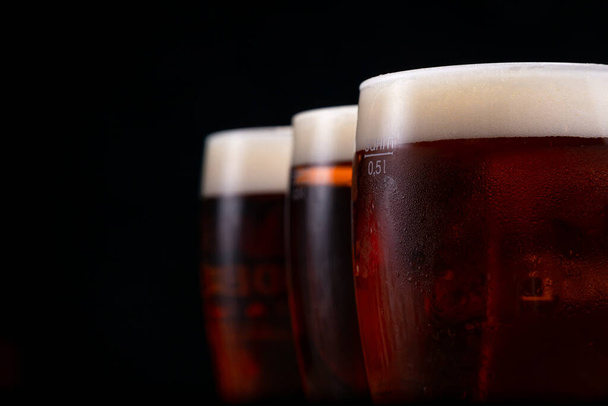 a glass of foamy beer on a dark background - Foto, Imagen