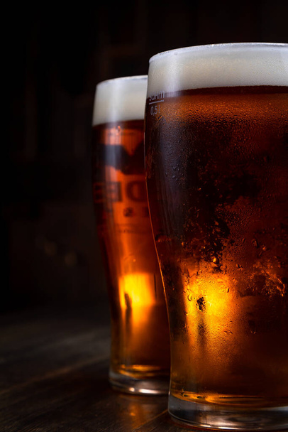 a glass of foamy beer on a dark background - Фото, изображение