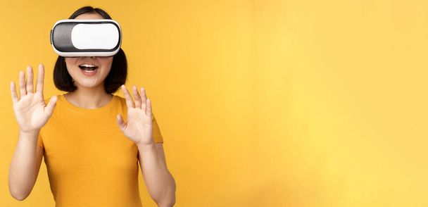 VRで遊んでいる若いアジア人女性,仮想現実のメガネを使用して,スタジオの背景に黄色のTシャツを着て - 写真・画像
