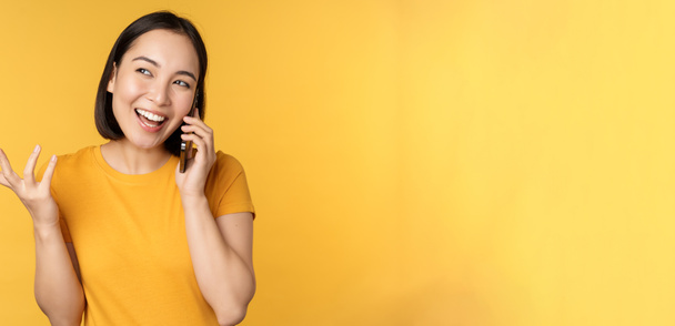 Una giovane coreana che parla al cellulare. Asiatico donna chiamata su smartphone, in piedi su sfondo giallo - Foto, immagini