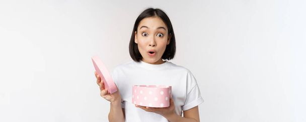 Happy aziatische vrouw, vriendin open doos met Valentijnsdag cadeau, ontvangen romantisch cadeau, staande over witte achtergrond - Foto, afbeelding